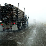 logging truck driving through snow blizzard road conditions