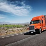 orange semi truck driving on road through desert