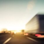 blurry image of truck driving on road toward sunset