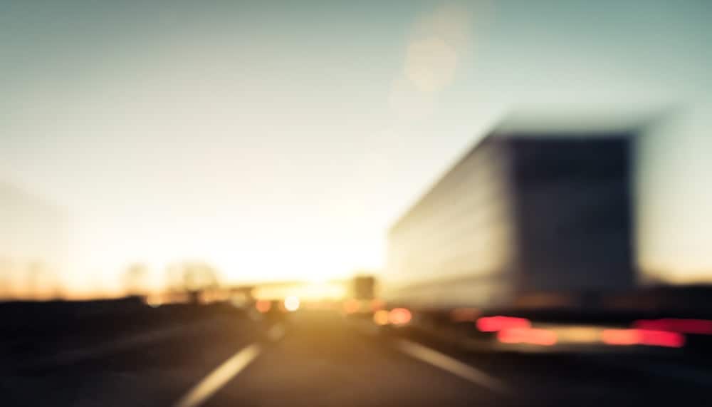 blurry image of truck driving on road toward sunset