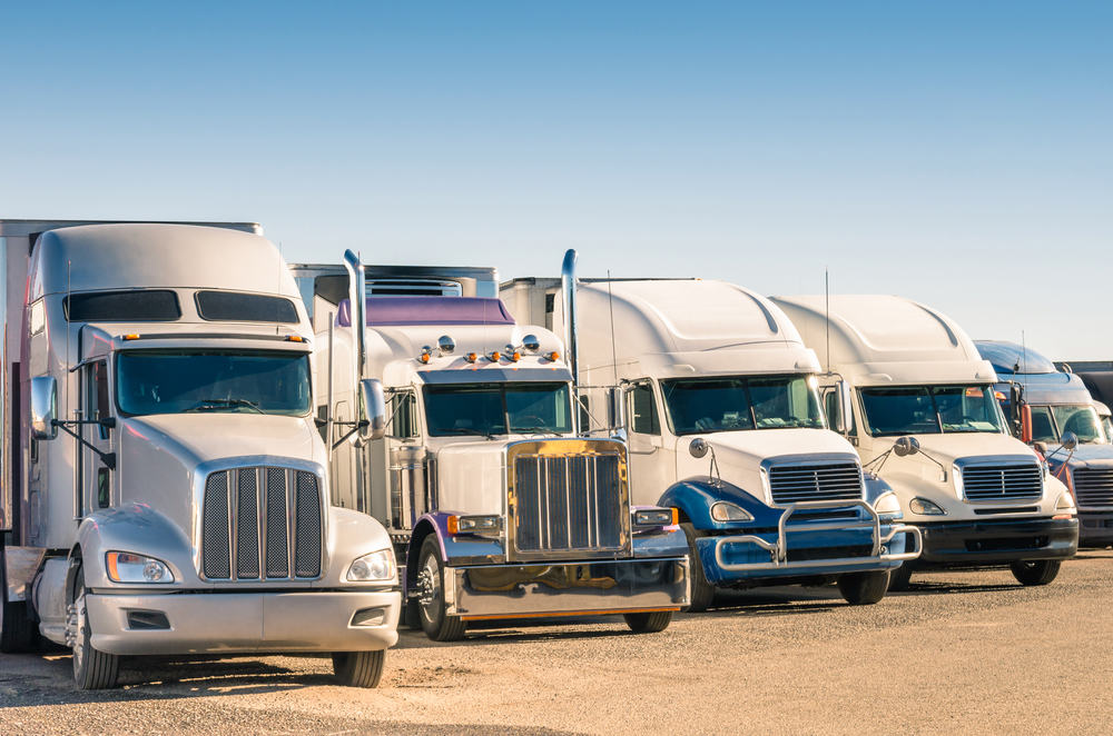 five semi trucks lined up parked in a lot