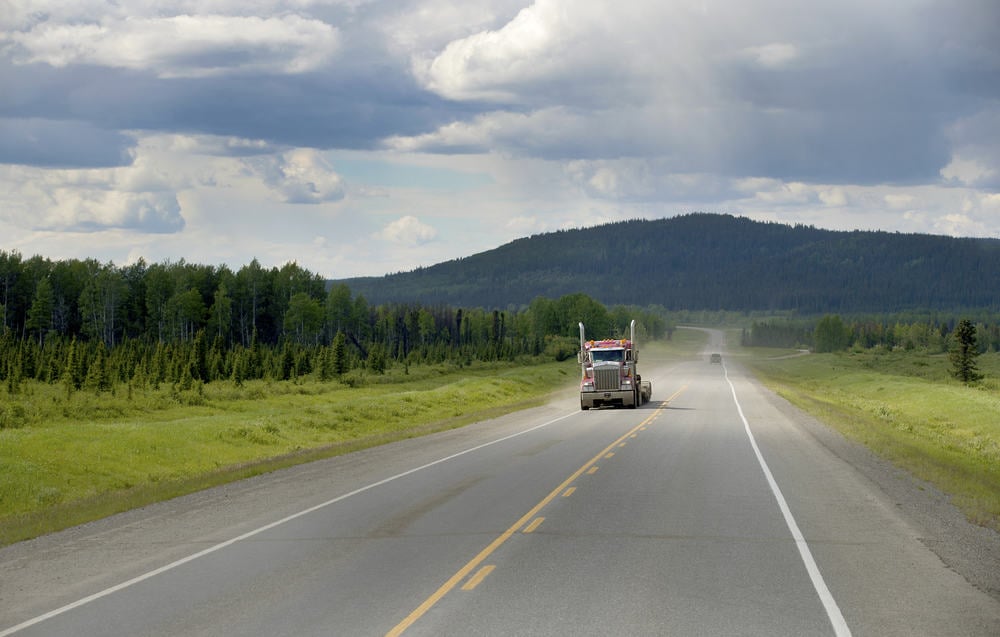 semi driving on road near evergreen trees
